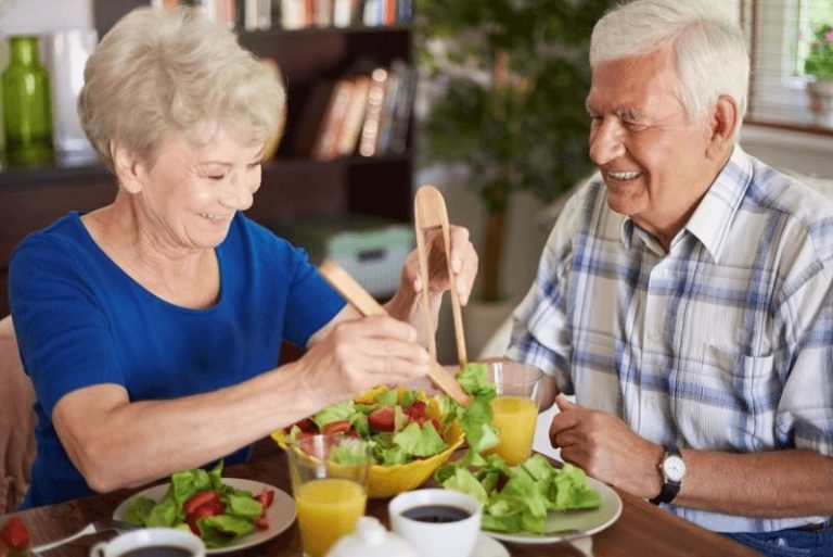 Couple de séniors heureux mangeant une salade, devant faire attention à leur alimentation