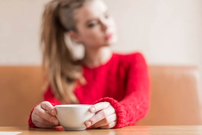 Une jeune femme observe sa tasse de thé avec interrogation.