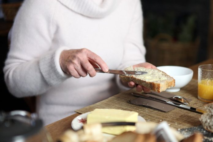 manger du beurre risques maladies chroniques cardiovasculaires Ma Santé Une femme qui tartine son pain avec du beurre au petit déjeuner.