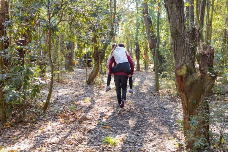 Vue arrière d'homme portant sa copine sur le dos et en marchant dans la forêt.