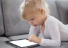 “Ipad kids” : quand les écrans prennent la place des mots Petite fille qui joue avec un iPad en étant allongée sur un canapé.