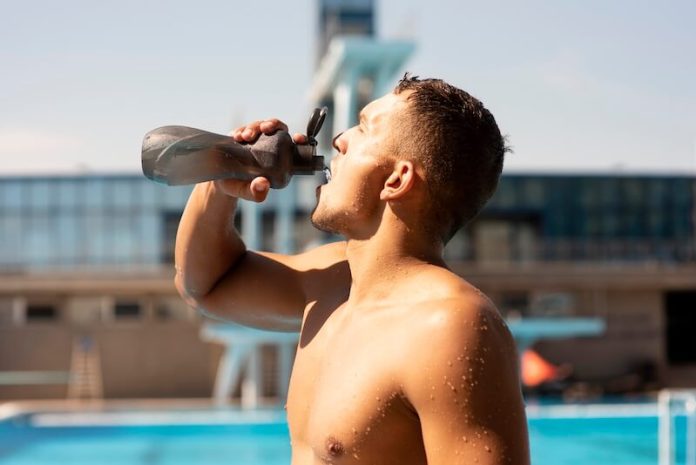 hydratation milieu aquatique ma sante Vue de côté d'un nageur qui boit de l'eau au bord d'une piscine pour rester hydraté.