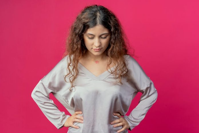 perimenopose femme 35 ans ma sante Femme qui regarde vers le bas, les mains sur les hanches.