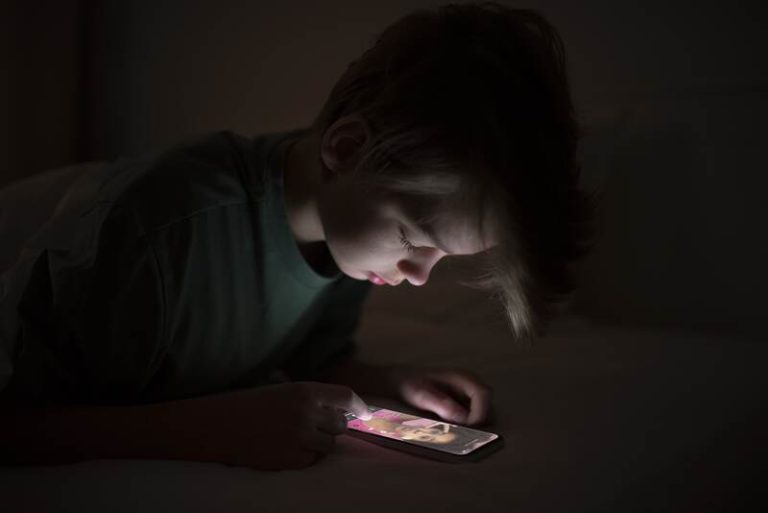 Un jeune adolescent accro à TikTok sur son téléphone en pleine nuit.