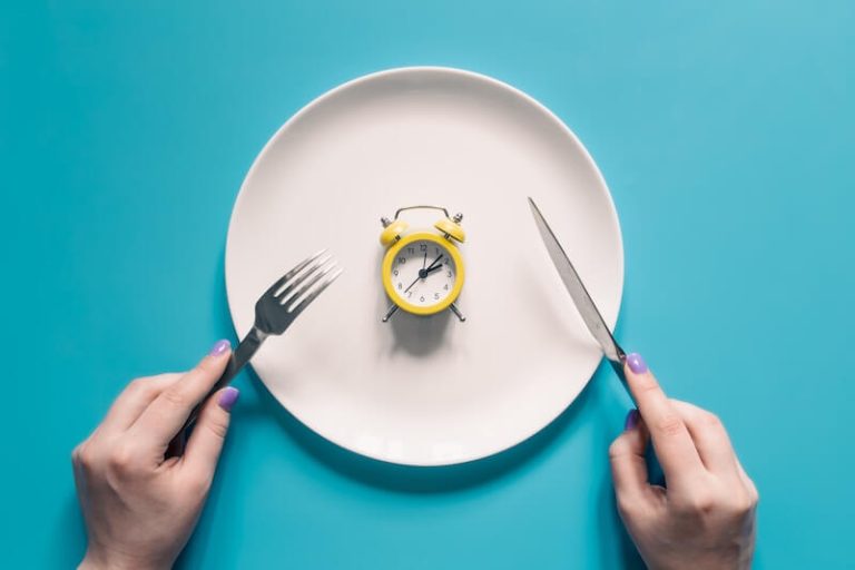 mains tenant une fourchette et un couteau au dessus d'un réveil dans une assiette.