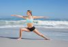 Sport : le top 4 des activités physiques à pratiquer à la plage Une jeune femme faisant des étirements sur le sable, face à la mer.