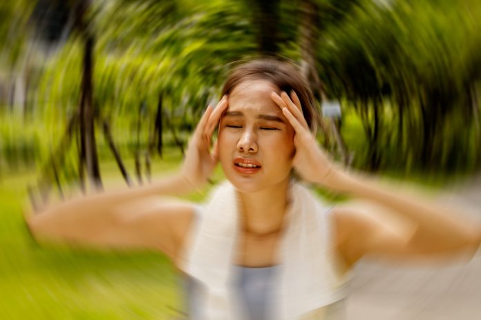 Asian woman exercising outdoors with discomfort hands gently massaging her head in too hot weather feeling sick dizzy fainting cerebral ischemia. Tired, supporting the body from slipping. Une femme en train de faire un malaise à cause de la prise de ses médicmants en période de chaleur caniculaire.