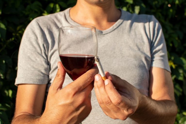 Un homme qui boit du vin rouge en fumant une cigarette.