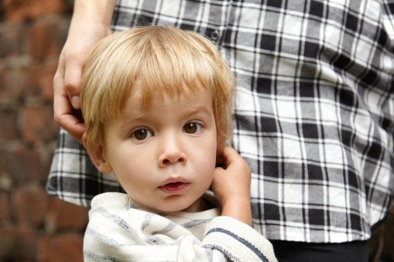 Un enfant, dans les jupes de sa mère, agacé de bégayer et de ne pas réussir à se faire comprendre.