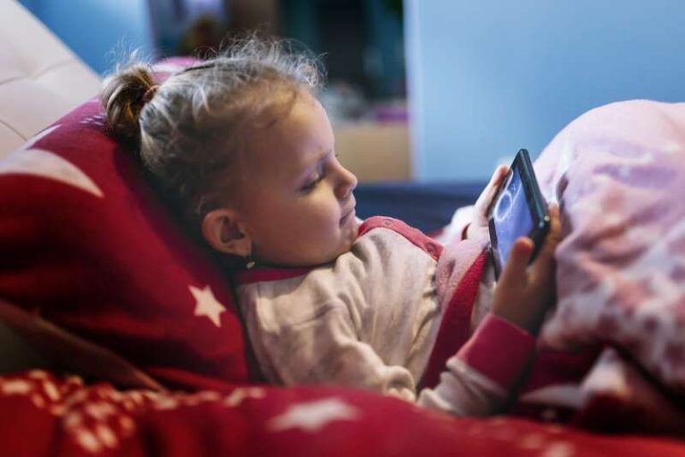 Une enfant les yeux rivés sur le téléphone d'un de ses parents.