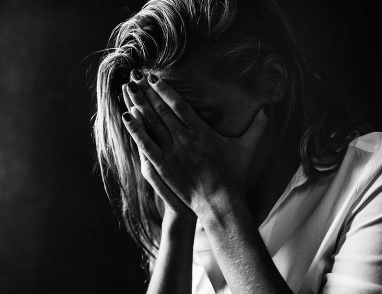 Une femme qui se prend la tête dans les mains, rongée par l'anxiété.