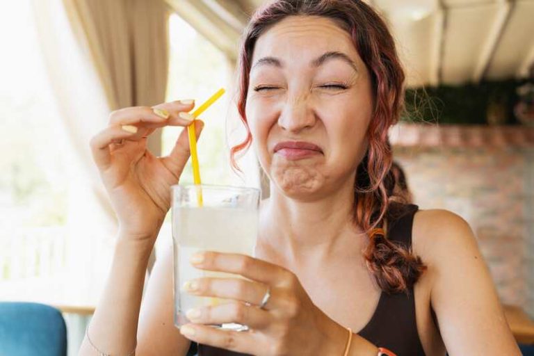 Une femme en train de boire un verre et qui a soudainement un mauvais goût de fer dans la bouche.