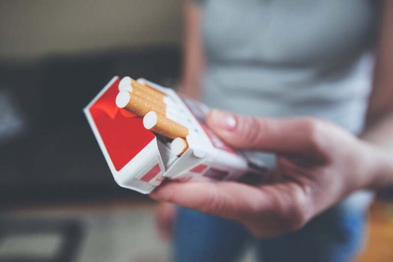 Une femme montre la marque de son paquet de cigarettes, l’une de celles appelées à disparaître en 2026.