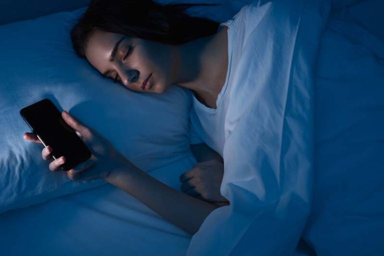 Une femme qui dort avec son téléphone pour détecter les symptômes d'une apnée du sommeil.