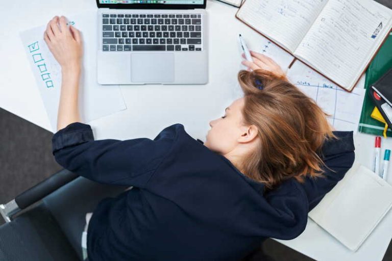 Une femme, allongée sur son bureau, qui est allée au travail en étant malade.