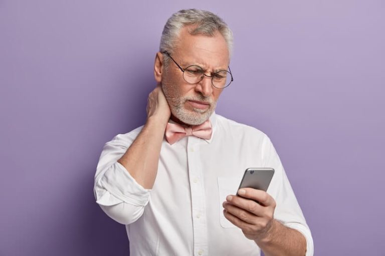 Un homme penché sur son téléphone avec une douleur derrière la nuque soupçonnant un début de "Text Neck".