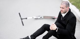 Ligament croisé : une rupture sans douleurs est-elle possible ? Un homme freinant en trottinette qui bloque son pied sur le sol, provoquant une torsion brutale du genou qui a rompu le ligament.
