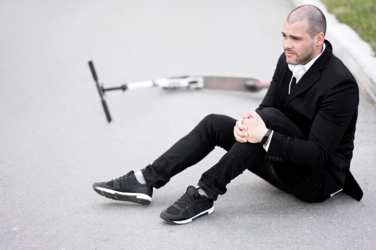 Un homme freinant en trottinette qui bloque son pied sur le sol, provoquant une torsion brutale du genou qui a rompu le ligament.