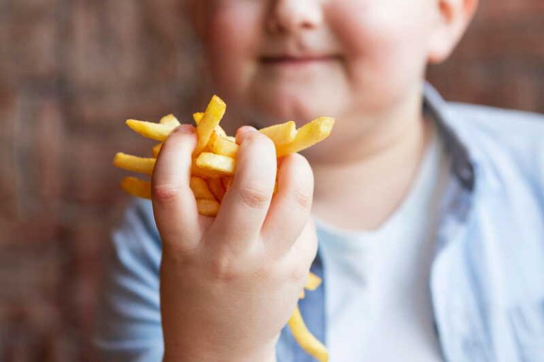 Un enfant en situation d’obésité tenant des frites dans les mains, faute d’avoir été sensibilisé au bien manger.