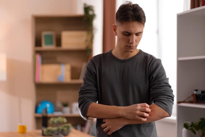 plaques rouges peau causent des symptômes démangeaison ma sante Un homme se gratte le bras en raison de démangeaisons, après avoir remarqué une rougeur suspecte sur la peau.