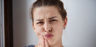 Aphtes à répétition : comment réagir pour éviter la récidive ? Une femme se tord de douleur en se tenant la joue, gênée par un aphte douloureux dans la bouche.