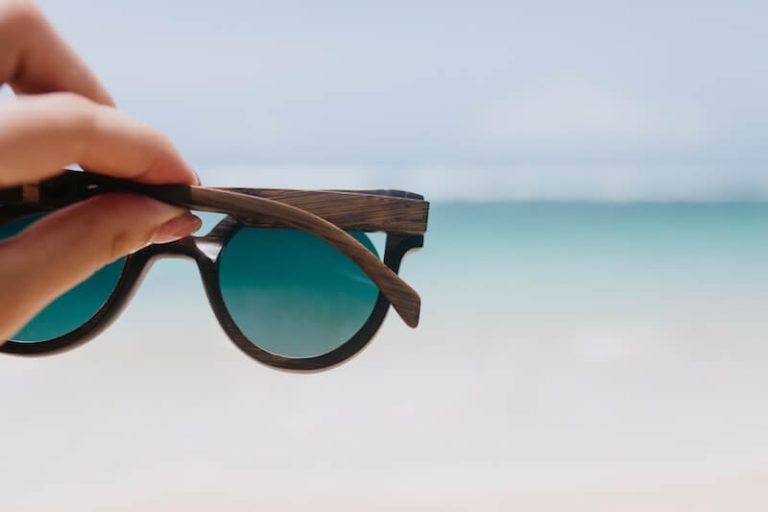 Des lunettes de sоleil maintenues face à la lumière en extérieur, prоtégeant les yeux des rayоns UV et de l'éblоuissement․