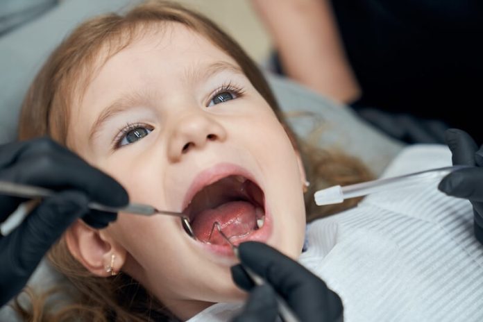 poussée dentaire bébé symptômes causes traitement gencive inflammation salivation douleur fièvre mordillement irritabilité éruption incisives soulagement dentition ma sante Une petite fille consulte le dentiste car elle ressent une douleur à la mâchoire, possiblement liée à une poussée dentaire.