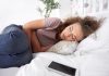 Une femme allongée sur son lit se tient le ventre, ressentant des douleurs et des ballonnements abdominaux, suspectant être atteinte d'un cancer de l'intestin grêle.