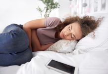 Troubles du transit : les signes d’un cancer de l’intestin grêle ? Une femme allongée sur son lit se tient le ventre, ressentant des douleurs et des ballonnements abdominaux, suspectant être atteinte d'un cancer de l'intestin grêle.
