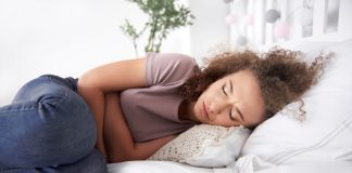Troubles du transit : les signes d’un cancer de l’intestin grêle ? Une femme allongée sur son lit se tient le ventre, ressentant des douleurs et des ballonnements abdominaux, suspectant être atteinte d'un cancer de l'intestin grêle.