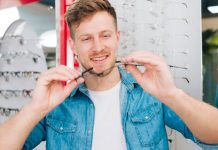 Lunettes : comment bien choisir sa monture selon la forme de son visage ? Un homme essaie des lunettes adaptées à la forme de son visage, avec les conseils d’un opticien.