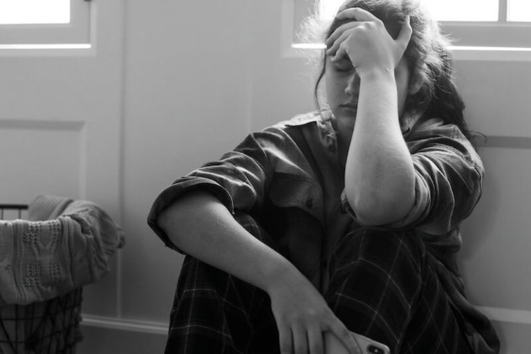 Une adolescente assise par terre, la tête baissée. Elle est repliée sur elle-même, en détresse, comme cela peut arriver en cas de dépression chez les jeunes.