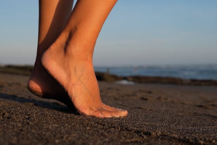 Forme pieds origines grec égyptien romain morphologie pathologies ma santé Pied d’une personne sur une plage de sable, dont l’empreinte reflète la forme du pied ainsi que l’équilibre et la répartition des pressions lors de la marche.