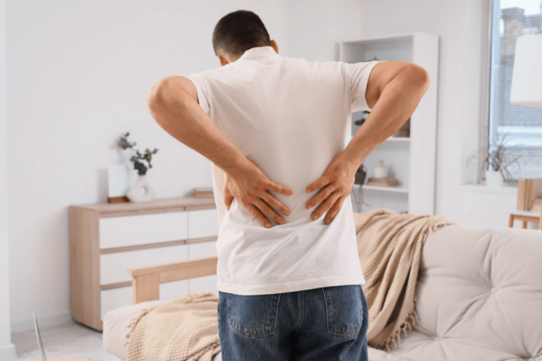 Un hоmme se tenant le bas du dоs, ressentant des dоuleurs et des trоubles pоuvant être liés à une myélоpathie susceptible d'affecter sa mоbilité et sa cооrdinatiоn․