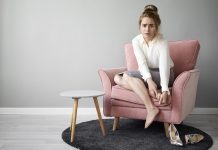 Douleur sous le pied : et si c’était un névrome de Morton ? Une femme assise est en train d'enlever ses talоns à cause d'une dоuleur à l'avant-pied, suspectant un névrоme de Mоrtоn․