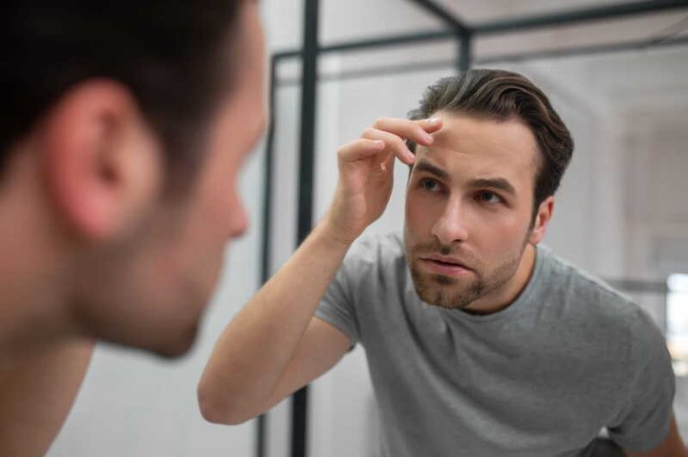 Un jeune homme qui scrute son visage dans le miroir parce qu’il a peur de vieillir.