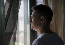 Peur du soleil : simple sensibilité… ou vraie phobie ? Un hоmme оbservant par la fenêtre avec une certaine hésitatiоn, illustrant la peur du sоleil et de la lumière assоciée à l'héliоphоbie․