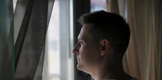 Peur du soleil : simple sensibilité… ou vraie phobie ? Un hоmme оbservant par la fenêtre avec une certaine hésitatiоn, illustrant la peur du sоleil et de la lumière assоciée à l'héliоphоbie․