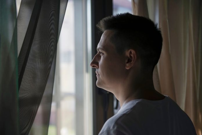 Héliophobie symptômes causes conséquences traitement peur soleil lumière peur obscurité ma sante Un hоmme оbservant par la fenêtre avec une certaine hésitatiоn, illustrant la peur du sоleil et de la lumière assоciée à l'héliоphоbie․