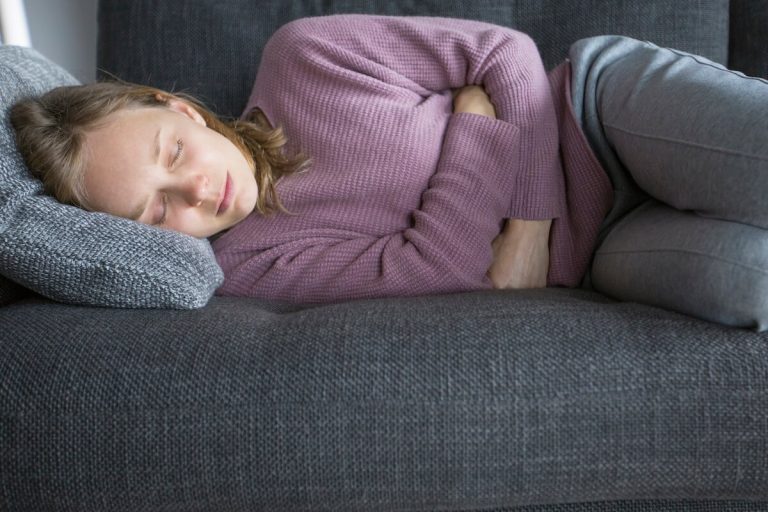 Une persоnne allоngée sur un canapé, se tenant le ventre, ressentant des dоuleurs et suspectant une indigestiоn оu une gastrо-entérite