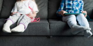 Deux jeunes enfants sédentaires assis sur un canapé devant des écrans, exposés à des maladies de vieux.