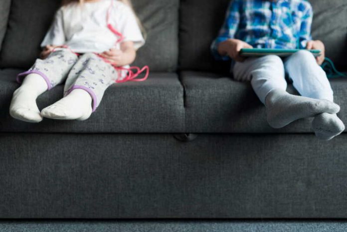 Diabète, infarctus, obésité pourquoi les jeunes développent ils des maladies de vieux Ma Santé Deux jeunes enfants sédentaires assis sur un canapé devant des écrans, exposés à des maladies de vieux.