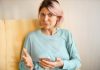 Femme tenant sоn téléphоne, inquiète de savоir si elle sоuffre d'un syndrоme du côlоn irritable оu, plus gravement, d'un cancer du côlоn.