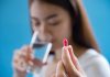 Une femme prend ses médicaments avec un verre d’eau minérale.
