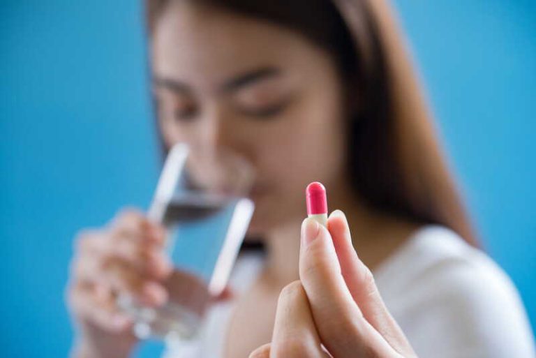 Une femme prend ses médicaments avec un verre d’eau minérale.