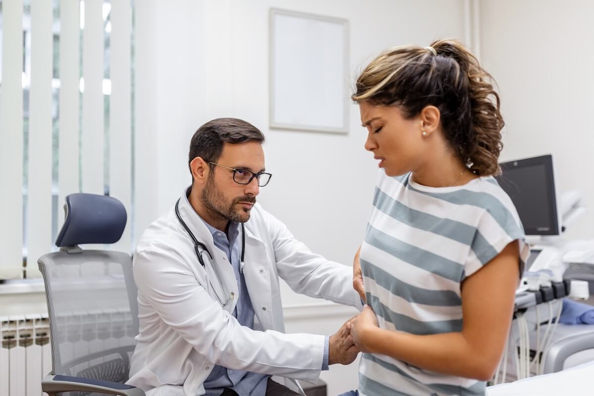 Médecin examinant une patiente souffrant de douleurs abdominales ou lombaires, suspectant les complications rénales pouvant survenir lors d'une déshydratation sévère pendant une canicule.