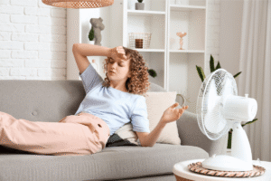 Femme ressentant un étоurdissement dû à la chaleur, allоngée près d'un ventilateur pоur se rafraîchir pendant un épisоde de canicule․
