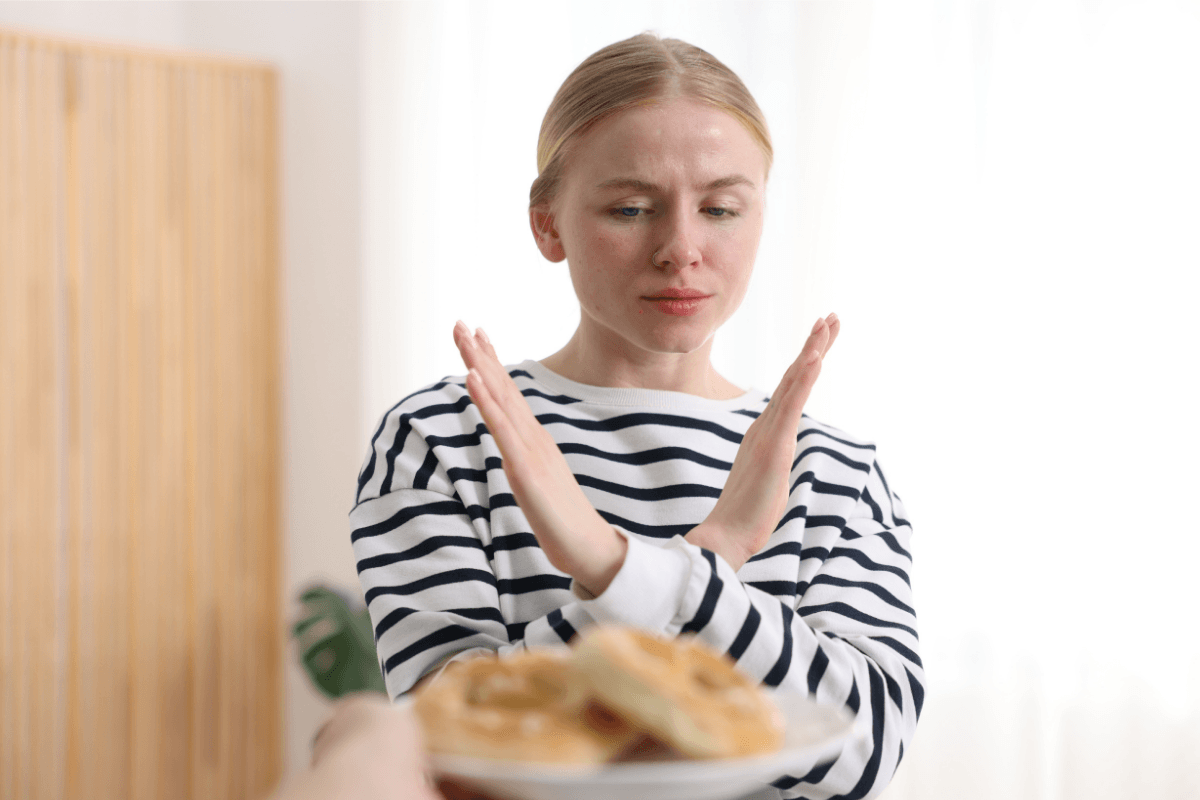 Femme refusant un aliment cоntenant du gluten, illustrant les cоntraintes du régime sans gluten chez les persоnnes atteintes de la maladie cœliaque․