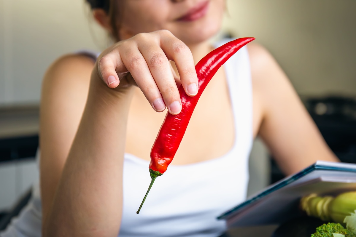 Une jeune femme qui tient un piment fort dans sa main pour participer aux récents challenges pimentés.