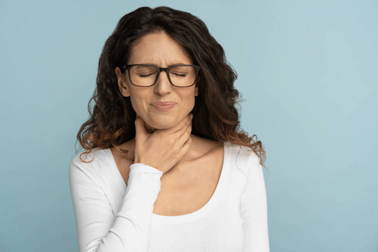 Une femme se tenant la gorge en raison d'une douleur importante à la déglutition, suspectant l'épiglottite.